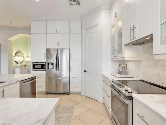 Kitchen with stainless steel appliances, white cabinetry, light tile patterned floors, light stone counters, and ornamental molding