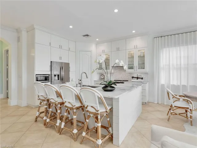 Kitchen featuring decorative backsplash, arched walkways, white cabinets, light stone counters, and a breakfast bar area