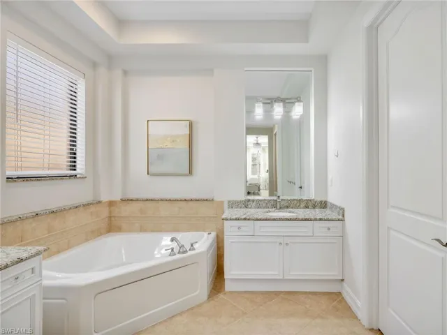 Full bathroom with vanity, a bath, light tile patterned flooring, and a tray ceiling