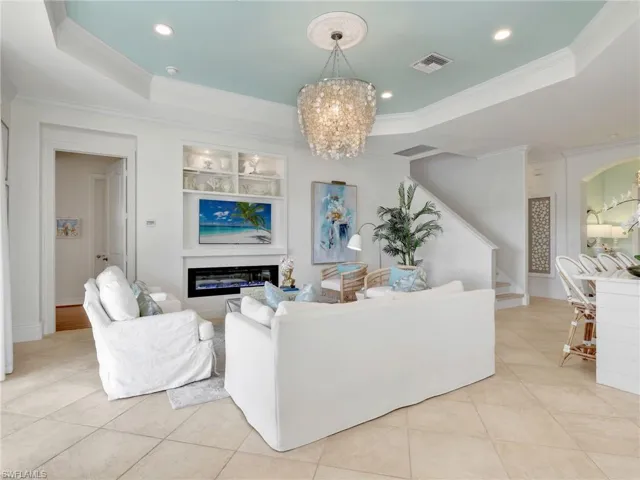 Living area with a raised ceiling, stairs, crown molding, a chandelier, and light tile patterned flooring