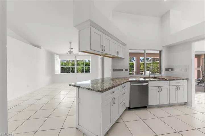 Kitchen featuring dark stone countertops, a peninsula, stainless steel dishwasher, light tile patterned floors, and a high ceiling