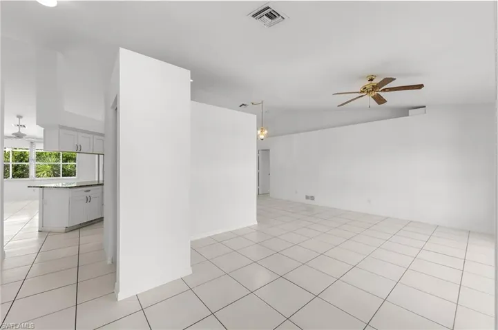 Empty room featuring ceiling fan, light tile patterned flooring, and vaulted ceiling