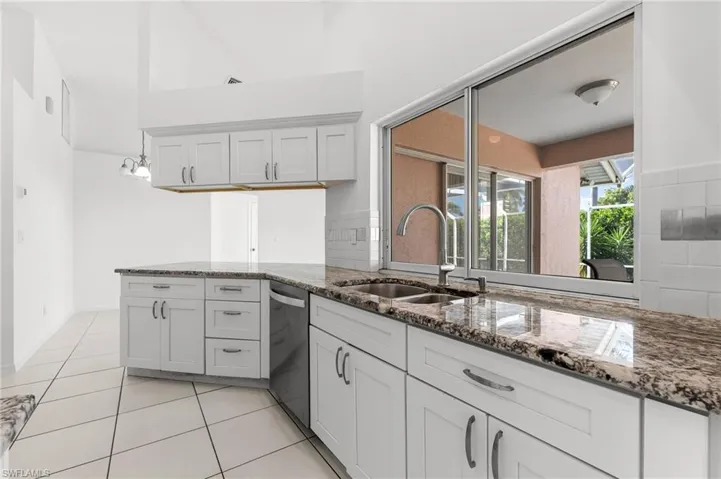 Kitchen featuring dark stone counters, light tile patterned floors, white cabinetry, and dishwasher