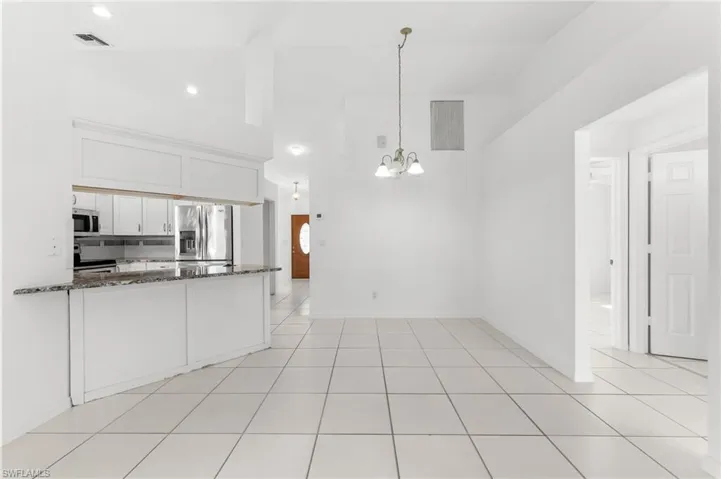 Kitchen with dark stone counters, white cabinetry, stainless steel appliances, hanging lights, and a peninsula