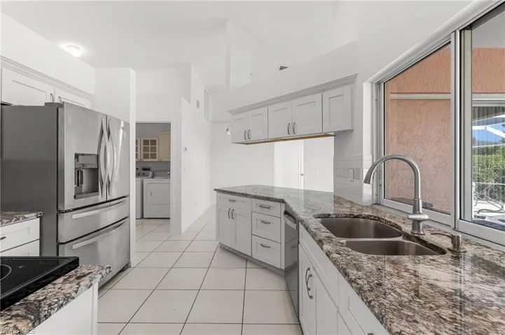 Kitchen with dark stone countertops, independent washer and dryer, stainless steel appliances, light tile patterned floors, and a high ceiling