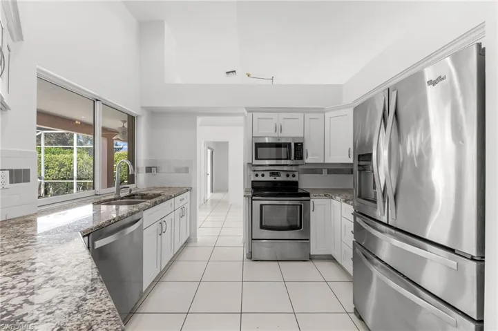 Kitchen featuring stainless steel appliances, light stone counters, white cabinetry, and a high ceiling