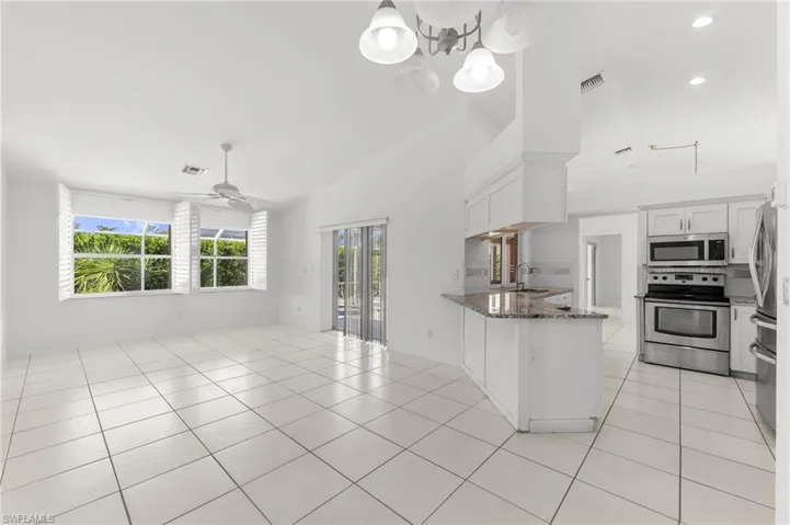 Kitchen featuring a peninsula, dark stone counters, stainless steel appliances, white cabinetry, and vaulted ceiling