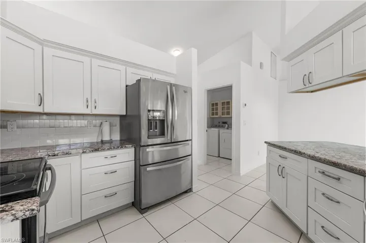 Kitchen featuring black electric range oven, independent washer and dryer, stainless steel fridge with ice dispenser, and light stone countertops