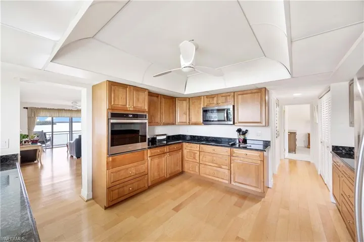 Kitchen featuring ceiling fan, stainless steel appliances, light wood-type flooring, and dark stone counters