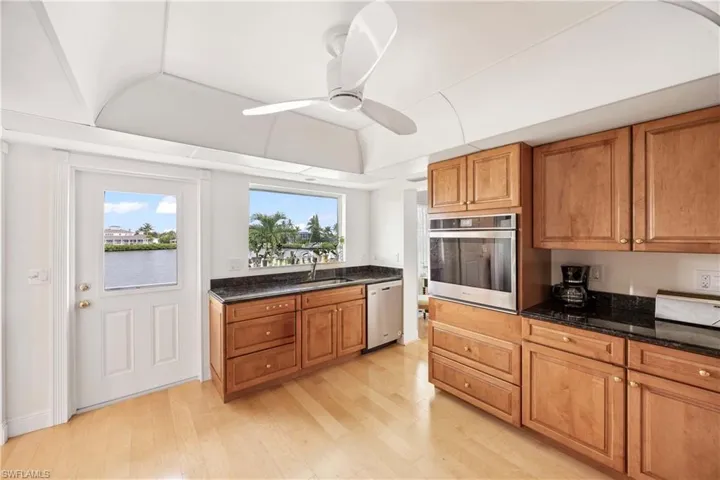 Kitchen featuring brown cabinetry, appliances with stainless steel finishes, dark stone counters, light wood-style flooring, and a ceiling fan