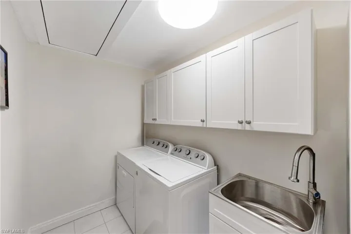 Washroom with cabinet space, light tile patterned floors, washer and dryer, and attic access