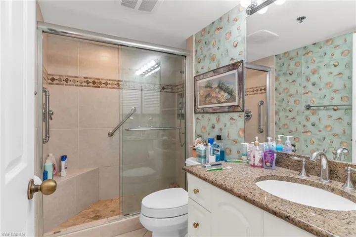 Bathroom featuring toilet, vanity, visible vents, a stall shower, and wallpapered walls