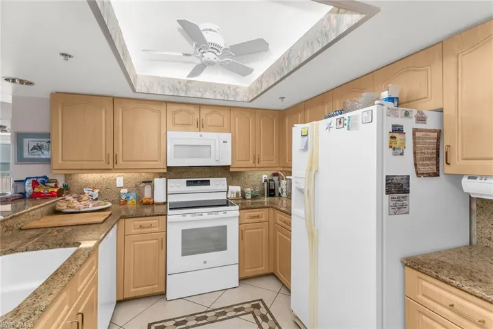 Kitchen featuring white appliances, light tile patterned floors, a tray ceiling, and light brown cabinetry