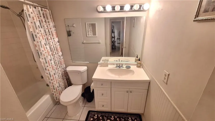 Full bath with shower / bathtub combination with curtain, vanity, a wainscoted wall, and light tile patterned flooring