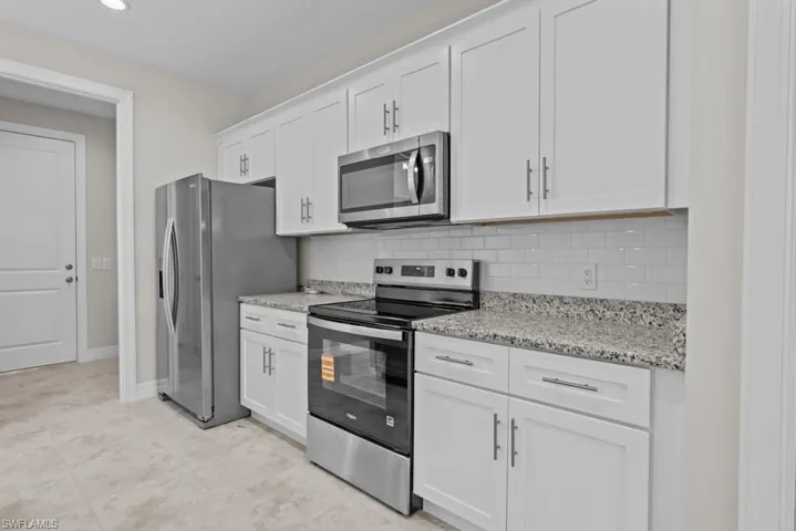 Kitchen featuring stainless steel appliances, white cabinetry, light stone countertops, and tasteful backsplash
