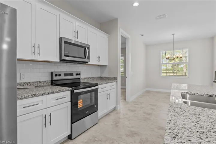 Kitchen featuring stainless steel appliances, white cabinetry, light stone counters, decorative backsplash, and hanging lights