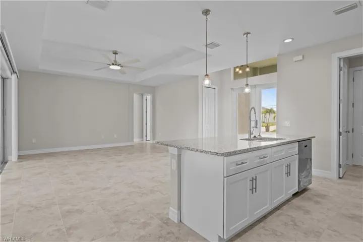 Kitchen featuring ceiling fan, a center island with sink, light stone countertops, hanging light fixtures, and open floor plan