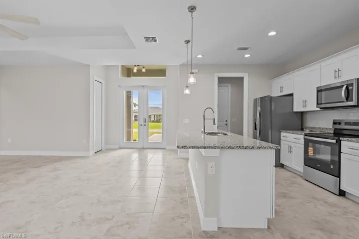 Kitchen with stainless steel appliances, french doors, light stone countertops, white cabinetry, and an island with sink