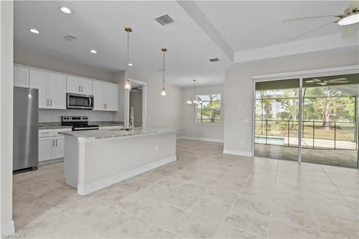 Kitchen featuring a ceiling fan, stainless steel appliances, white cabinetry, light stone counters, and a chandelier