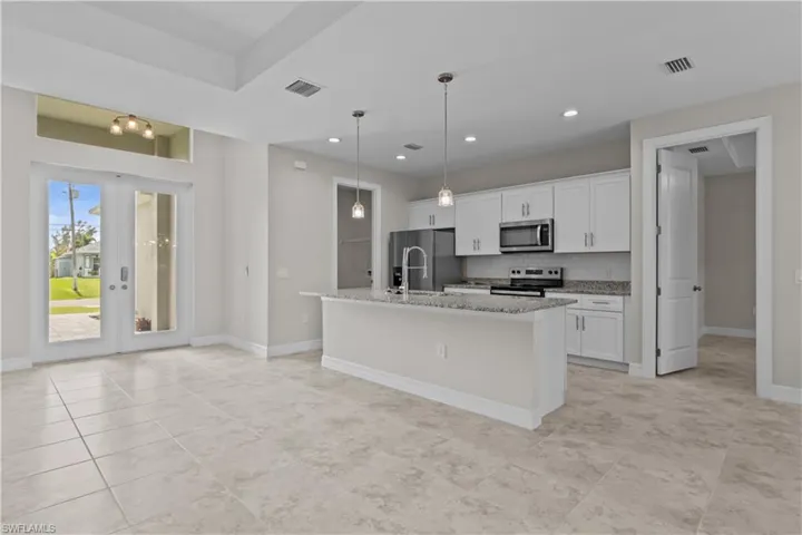 Kitchen featuring white cabinets, an island with sink, hanging light fixtures, light stone countertops, and stainless steel appliances