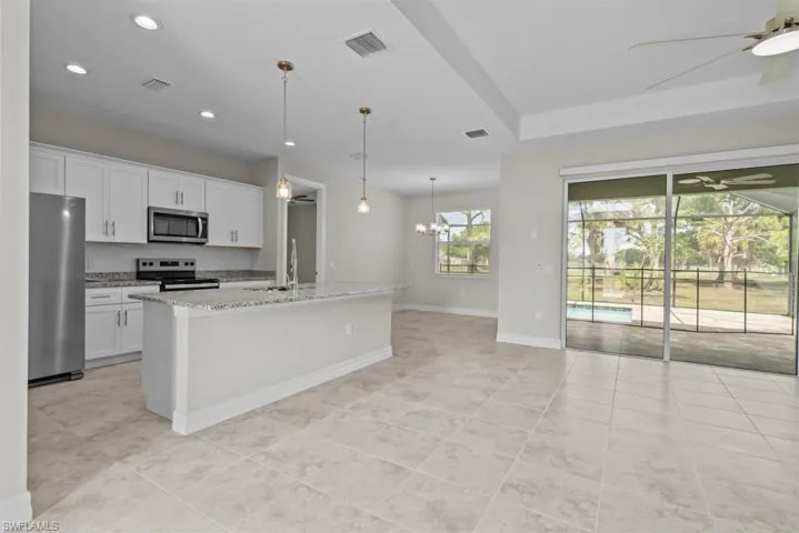 Kitchen with a ceiling fan, white cabinets, stainless steel appliances, light stone counters, and a center island with sink