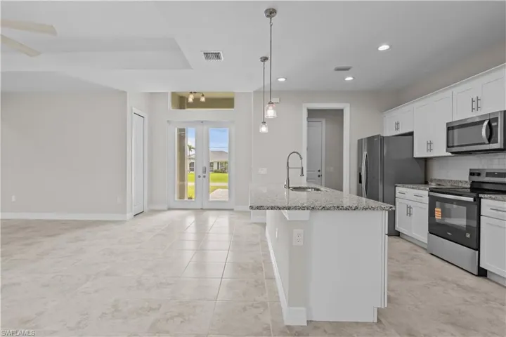 Kitchen featuring stainless steel appliances, french doors, light stone counters, white cabinets, and an island with sink