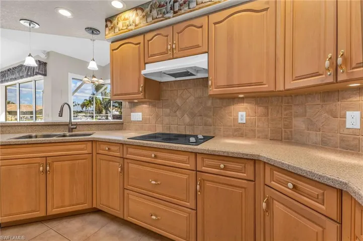 Kitchen featuring hanging light fixtures, backsplash, light tile patterned floors, light stone countertops, and a textured ceiling