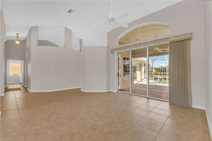 Empty room with ceiling fan, a sunroom, vaulted ceiling, and light tile patterned floors