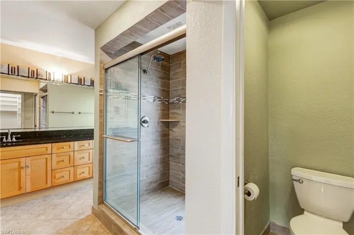 Bathroom featuring a textured wall, toilet, tile patterned floors, vanity, and a shower stall