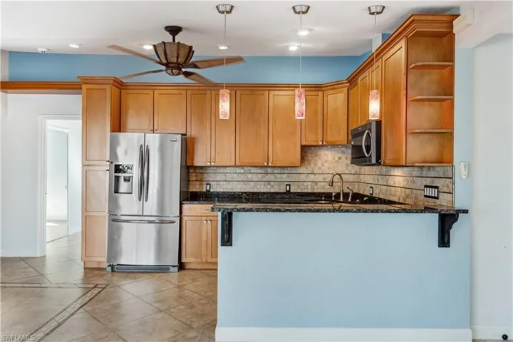 Kitchen featuring a peninsula, appliances with stainless steel finishes, backsplash, dark stone counters, and open shelves