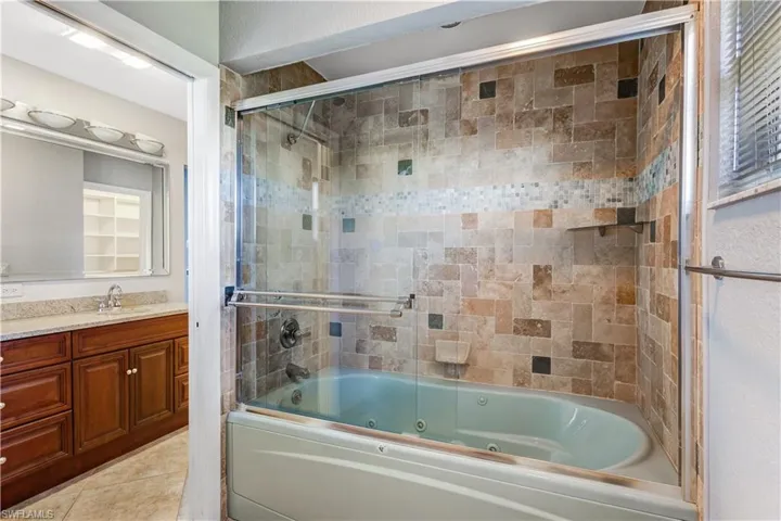 Bathroom with a combined bath / shower with jetted tub, vanity, and tile patterned floors