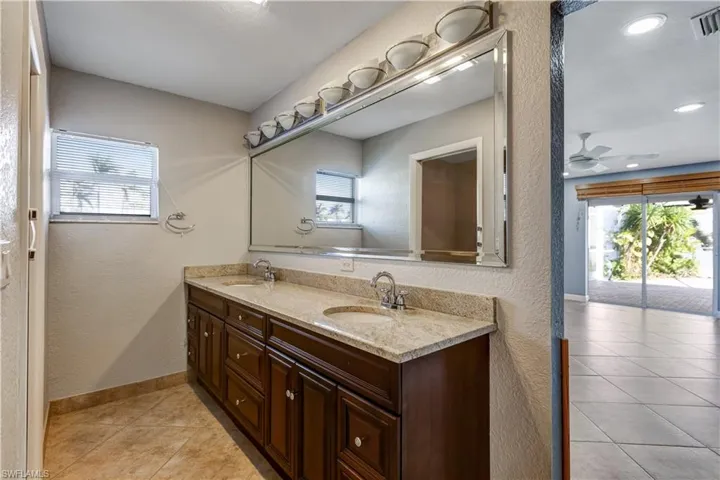 Full bathroom with a textured wall, double vanity, a sink, and baseboards