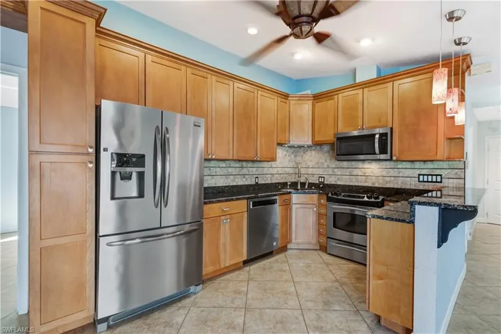 Kitchen with light tile patterned floors, decorative backsplash, appliances with stainless steel finishes, dark stone counters, and a peninsula