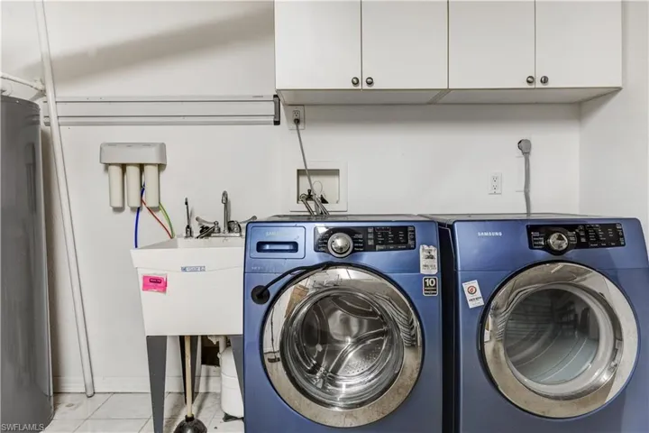 Laundry area with light tile patterned floors, separate washer and dryer, cabinet space, and water heater