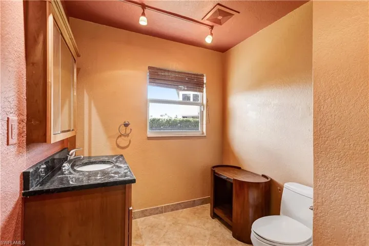 Half bath with baseboards, a textured wall, toilet, a textured ceiling, and vanity