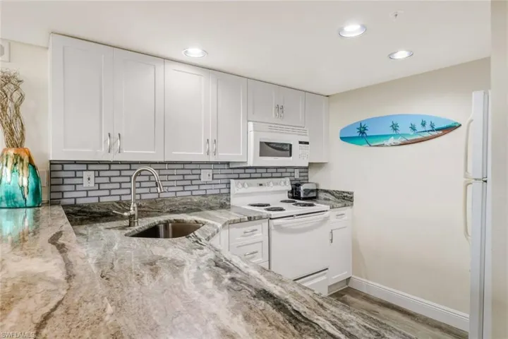 Kitchen featuring white cabinets, white appliances, light stone countertops, tasteful backsplash, and light wood-type flooring