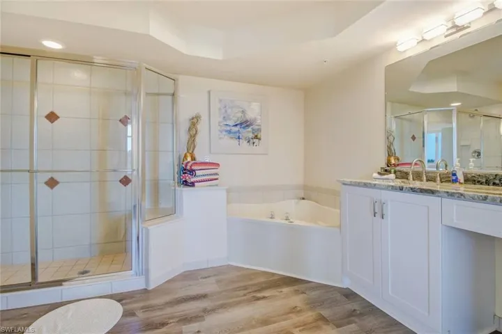 Full bathroom with vanity, a tray ceiling, a shower stall, a garden tub, and light wood-style flooring