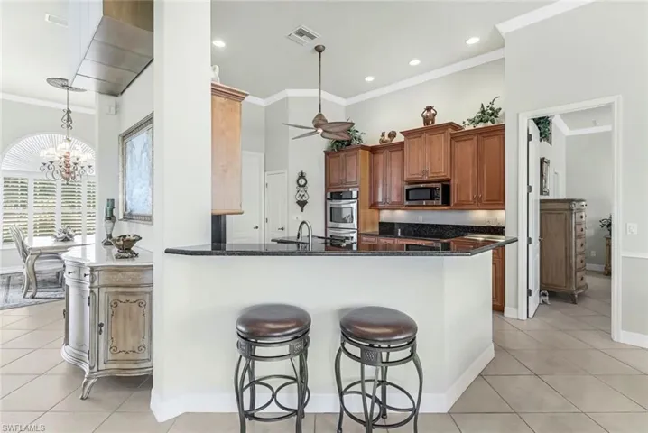 Kitchen with kitchen peninsula, stainless steel appliances, dark stone counters, light tile patterned floors, and ceiling fan with notable chandelier