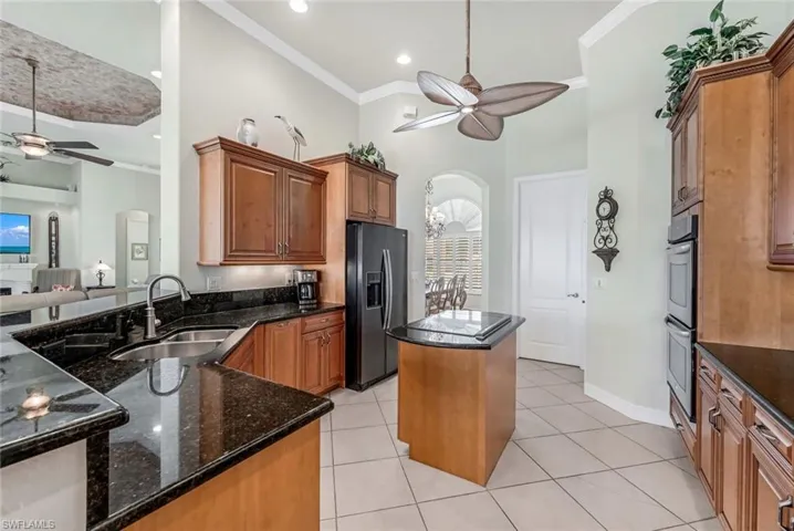 Kitchen featuring light tile patterned flooring, sink, a center island, kitchen peninsula, and black fridge
