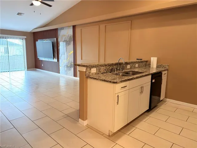 Kitchen featuring dark stone counters, a peninsula, white cabinets, lofted ceiling, and light tile patterned floors