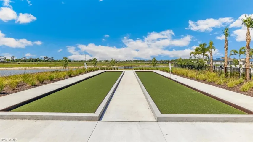 Outdoor bocce ball court featuring two green playing surfaces, a concrete path, and surrounding landscaping
