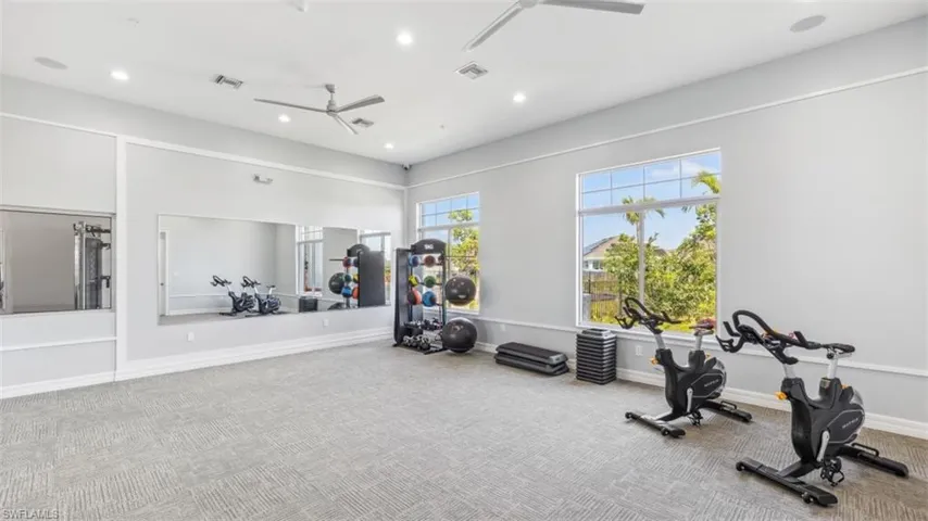 Fitness room featuring large windows, gray walls, light-colored carpet, ceiling fans, and a mirrored wall