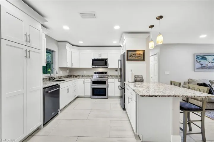 Kitchen with a kitchen breakfast bar, light stone countertops, white cabinets, a peninsula, and stainless steel appliances