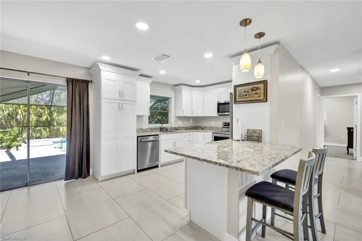 Kitchen with a peninsula, light stone counters, white cabinets, a breakfast bar, and appliances with stainless steel finishes