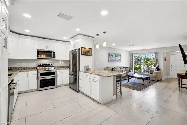 Kitchen with appliances with stainless steel finishes, light stone countertops, a kitchen bar, white cabinetry, and decorative light fixtures