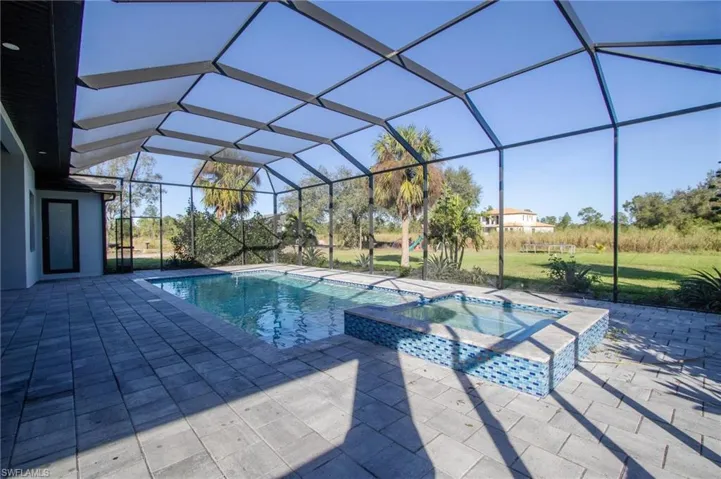 View of pool with an in ground hot tub, glass enclosure, and a patio area