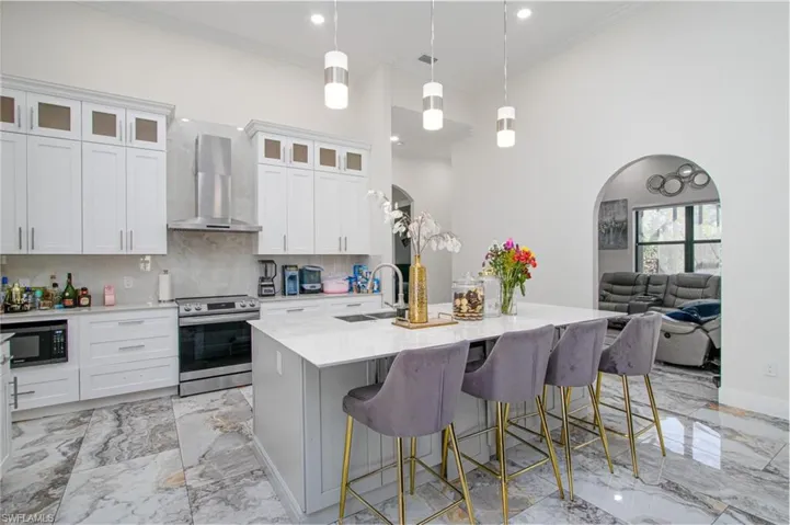 Kitchen featuring white cabinetry, hanging light fixtures, wall chimney range hood, electric stove, and a center island with sink