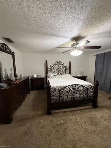 Carpeted bedroom featuring a textured ceiling, ceiling fan, and visible vents