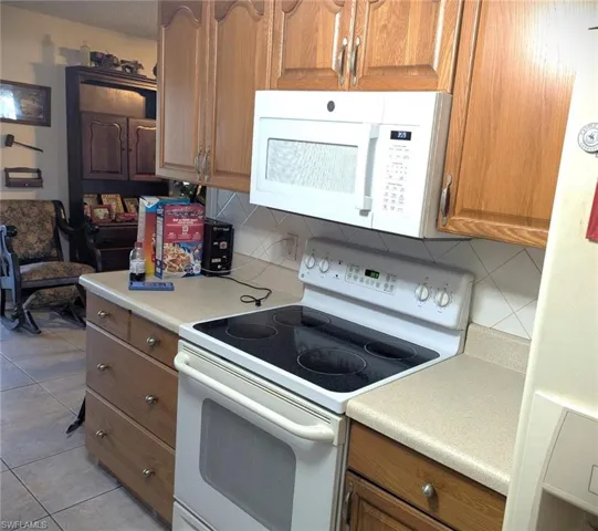 Kitchen with light tile patterned floors, white appliances, and decorative backsplash