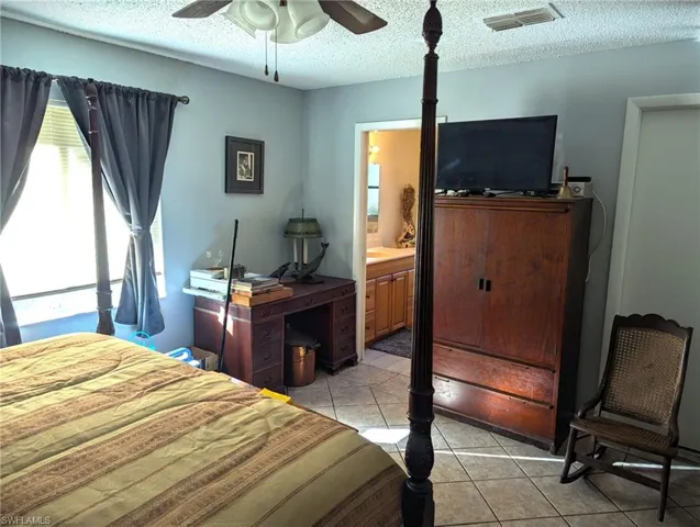 Bedroom with light tile patterned floors, ensuite bath, a textured ceiling, and ceiling fan
